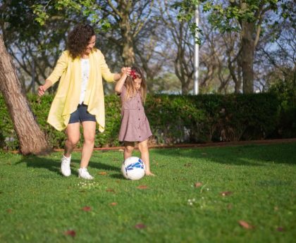 A mother and daughter enjoying a sunny day playing soccer in a lush green park.